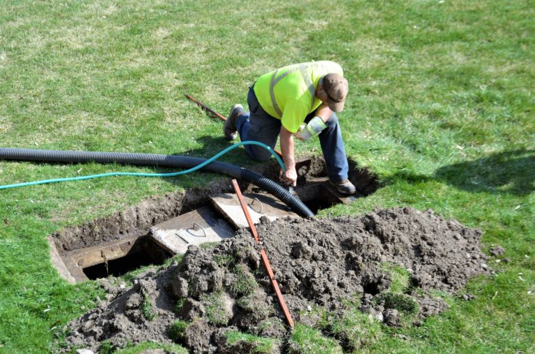 Technician kneeling over a dug-out septic tank to pump out waste